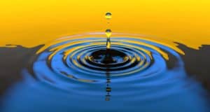 a drop of water lands in a smooth body of vibrant blue water with a vibrant color of golden horizon in the background